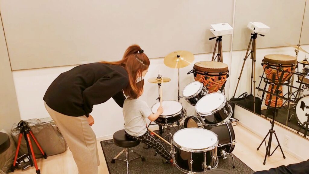 お母さんが不安で子供がドラムを叩くのに付き添っている様子